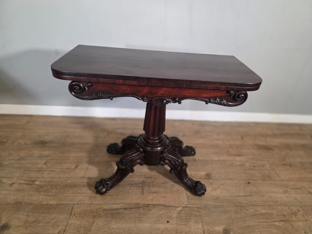 An antique early Victorian dark rosewood tea table featuring a fold-over top, carved scroll apron, and a central pedestal base with carved scroll feet. View II