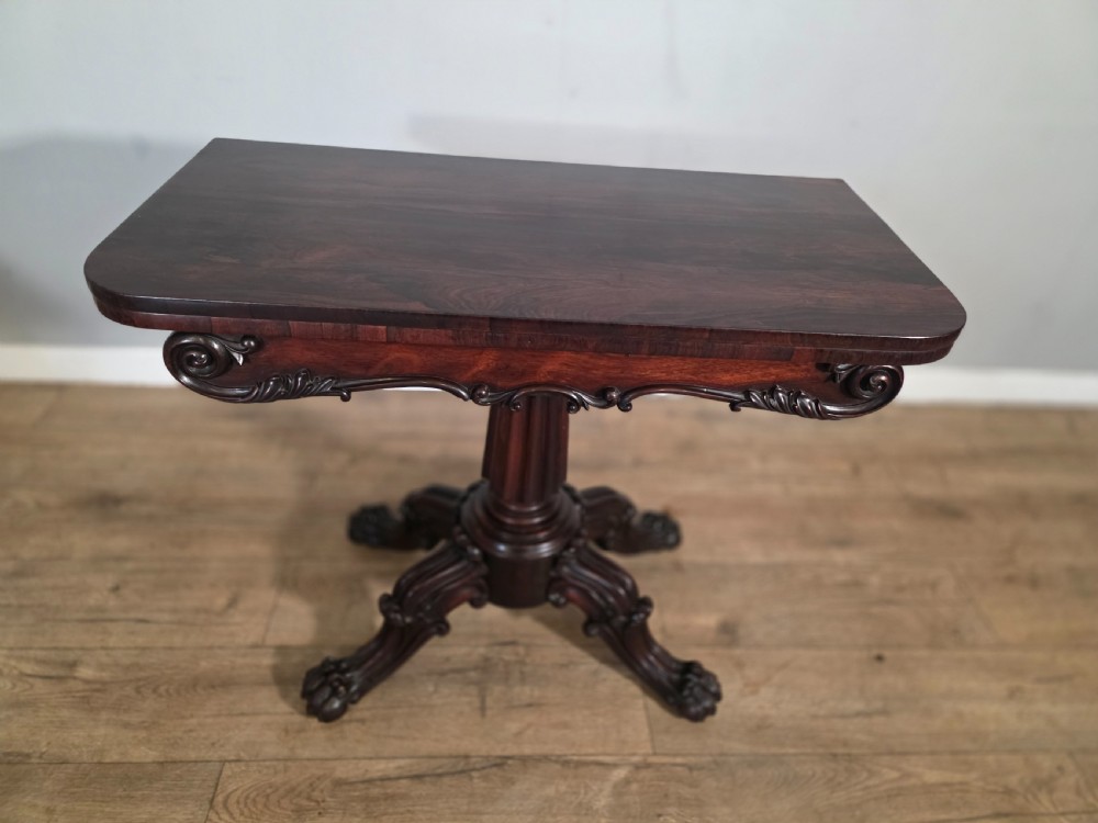 An antique early Victorian dark rosewood tea table featuring a fold-over top, carved scroll apron, and a central pedestal base with carved scroll feet. View III