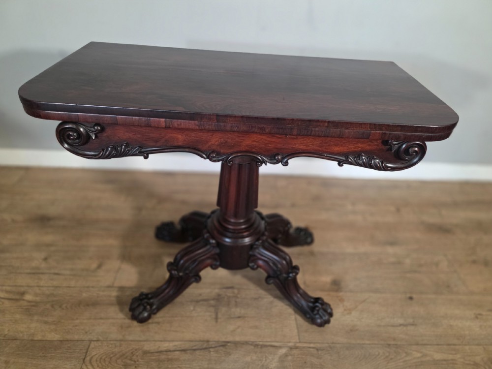 An antique early Victorian dark rosewood tea table featuring a fold-over top, carved scroll apron, and a central pedestal base with carved scroll feet. View VII