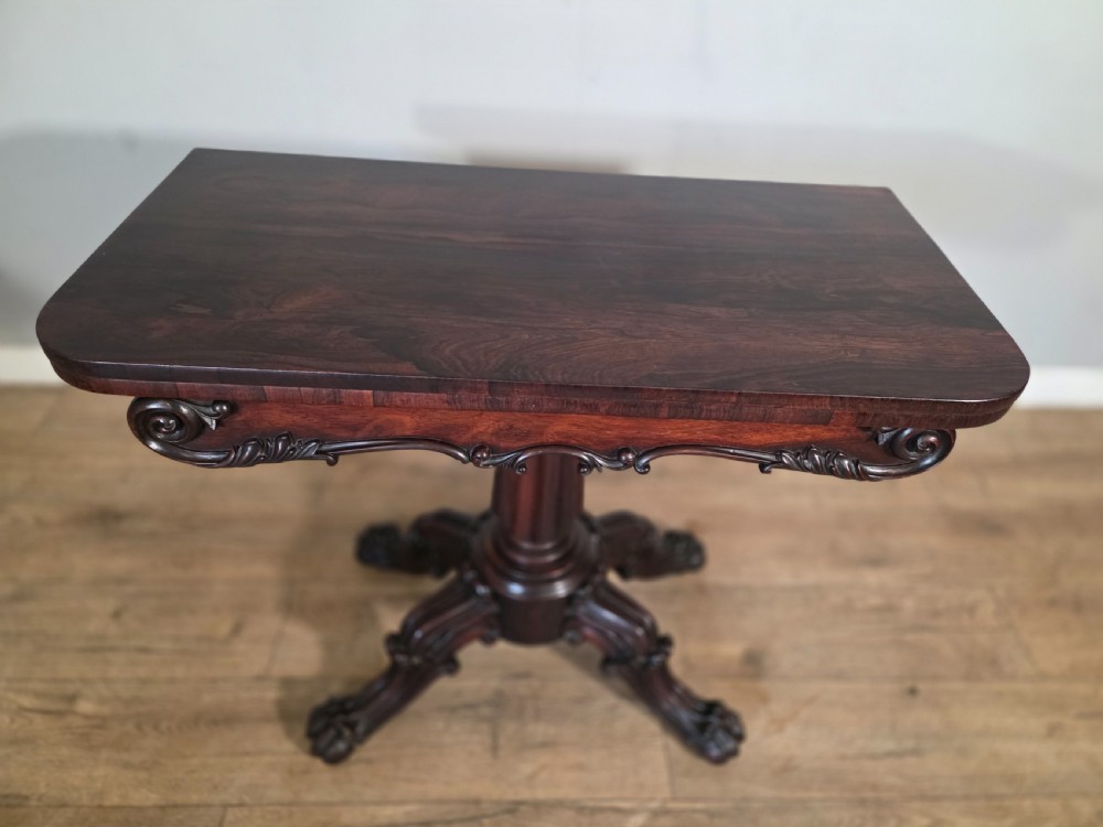 An antique early Victorian dark rosewood tea table featuring a fold-over top, carved scroll apron, and a central pedestal base with carved scroll feet. View VIII