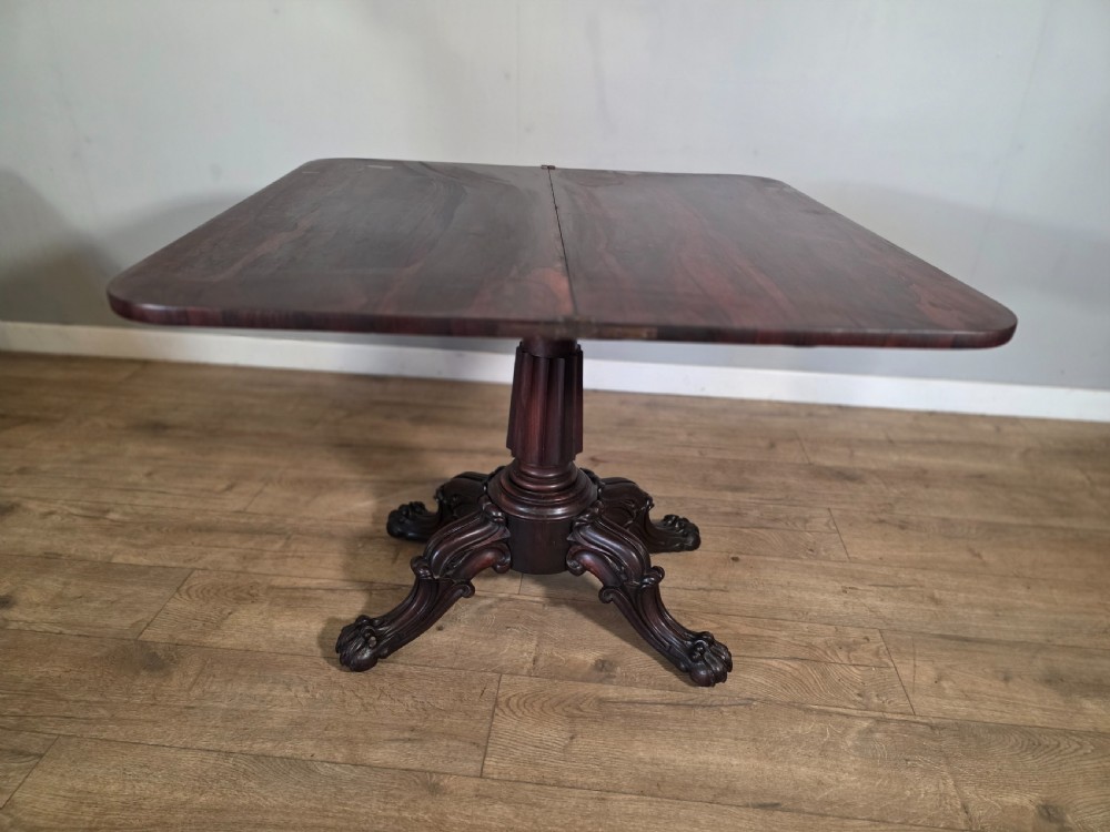 An antique early Victorian dark rosewood tea table featuring a fold-over top, carved scroll apron, and a central pedestal base with carved scroll feet. View XII