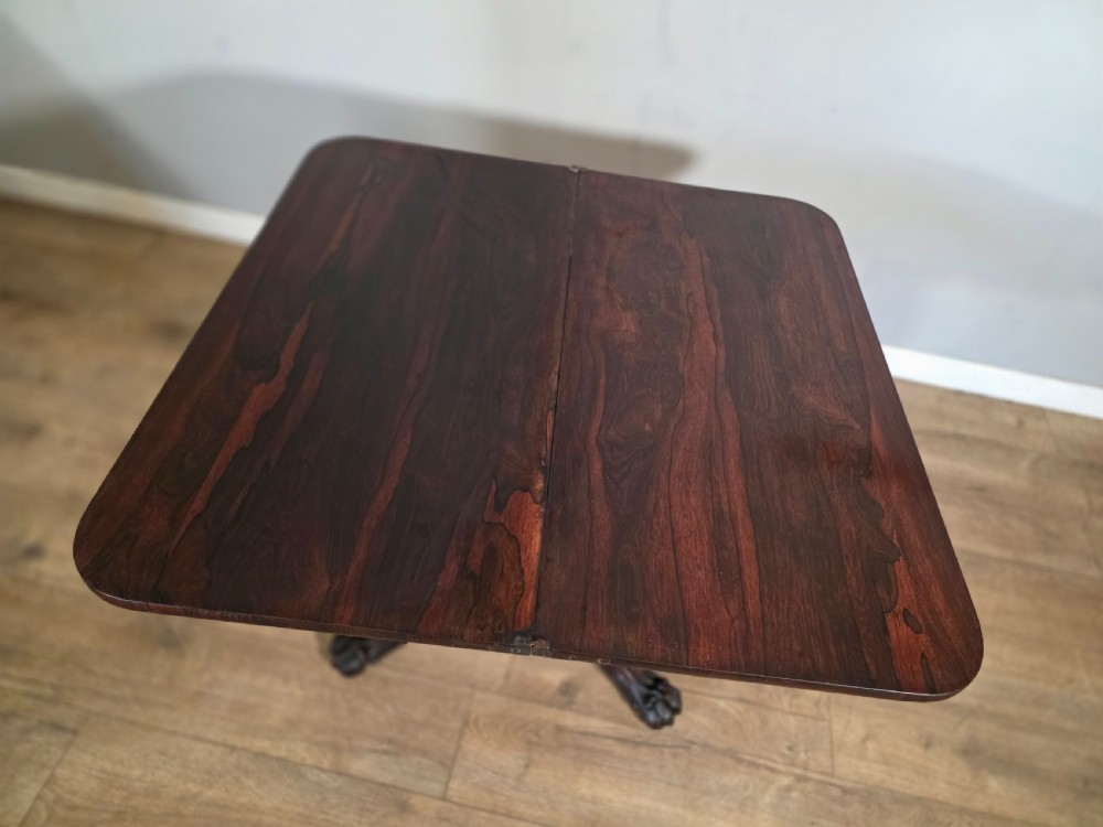 An antique early Victorian dark rosewood tea table featuring a fold-over top, carved scroll apron, and a central pedestal base with carved scroll feet. View XIII