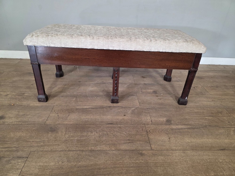 An 18th-century Adam style dark mahogany long window seat with six square tapered legs and a beige textured upholstered seat. View II