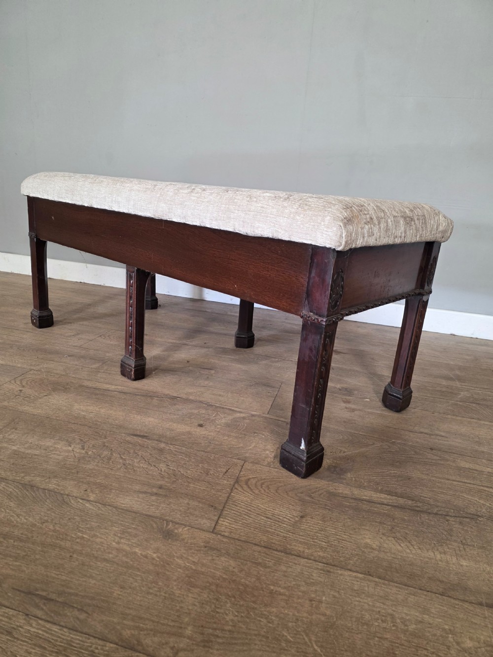 An 18th-century Adam style dark mahogany long window seat with six square tapered legs and a beige textured upholstered seat. View V