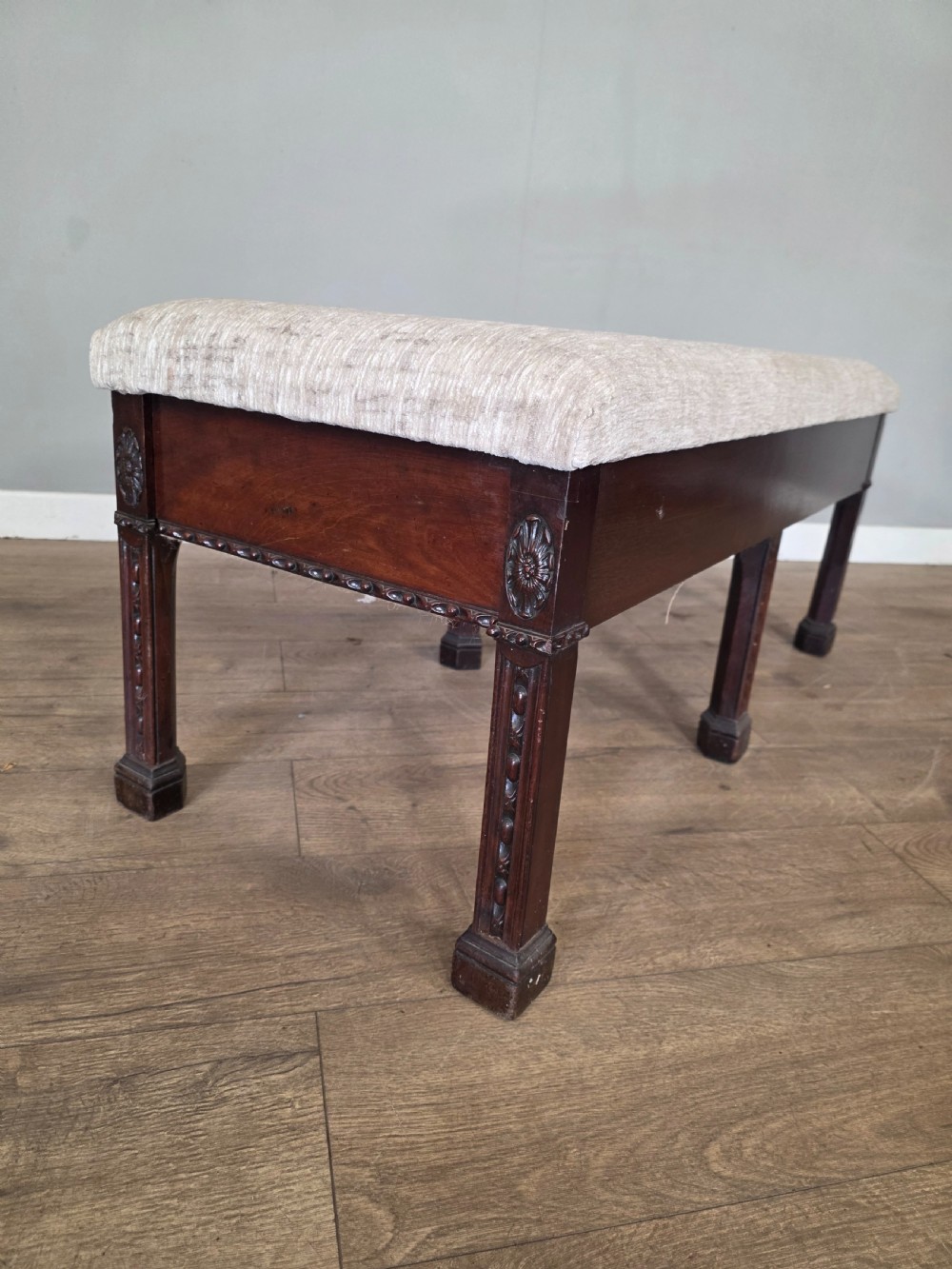 An 18th-century Adam style dark mahogany long window seat with six square tapered legs and a beige textured upholstered seat. View VI