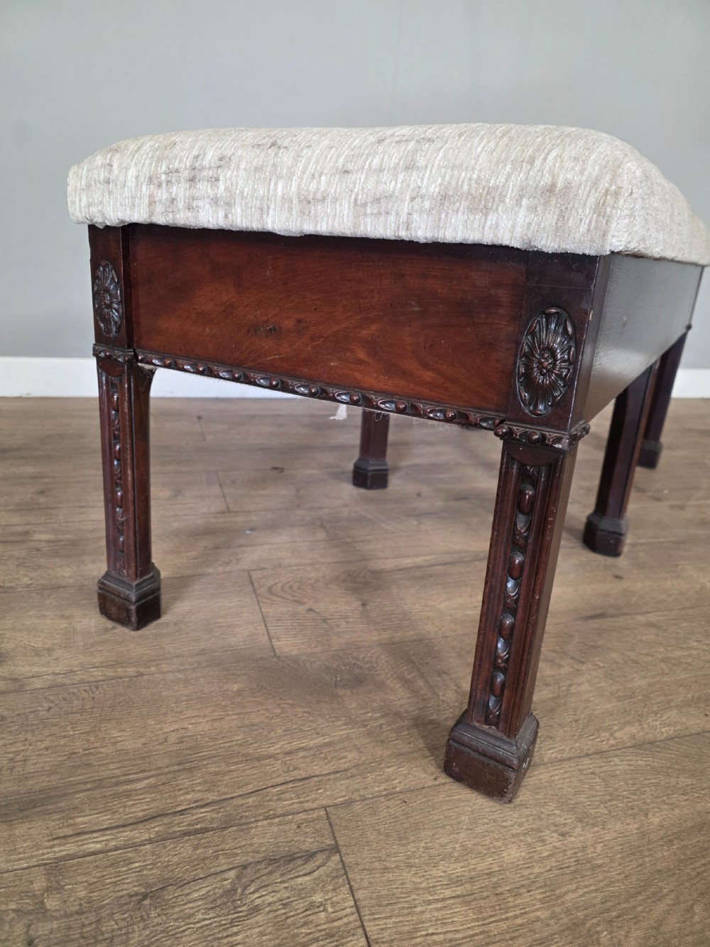 An 18th-century Adam style dark mahogany long window seat with six square tapered legs and a beige textured upholstered seat. View VII