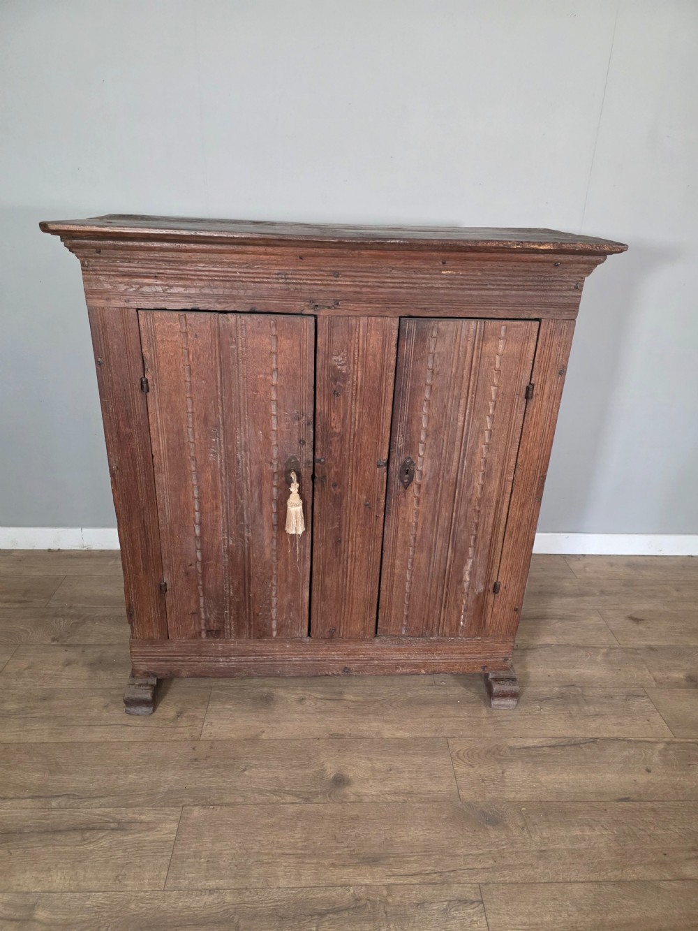 An 18th-century primitive dark oak cupboard featuring two panelled doors with notch carving, wrought iron escutcheons, and moulded top cornicing. View II