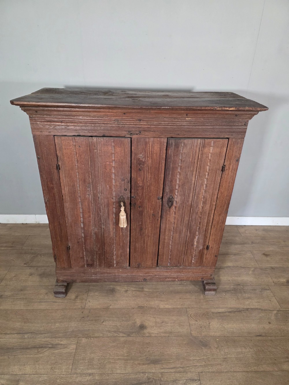 An 18th-century primitive dark oak cupboard featuring two panelled doors with notch carving, wrought iron escutcheons, and moulded top cornicing. View III