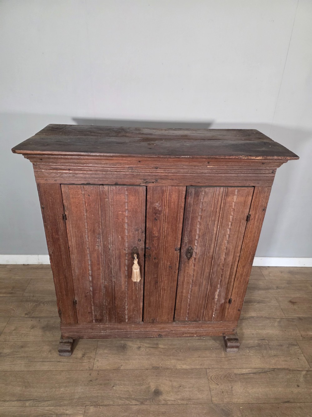 An 18th-century primitive dark oak cupboard featuring two panelled doors with notch carving, wrought iron escutcheons, and moulded top cornicing. View IV