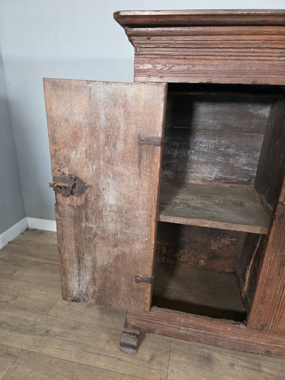 An 18th-century primitive dark oak cupboard featuring two panelled doors with notch carving, wrought iron escutcheons, and moulded top cornicing. View V