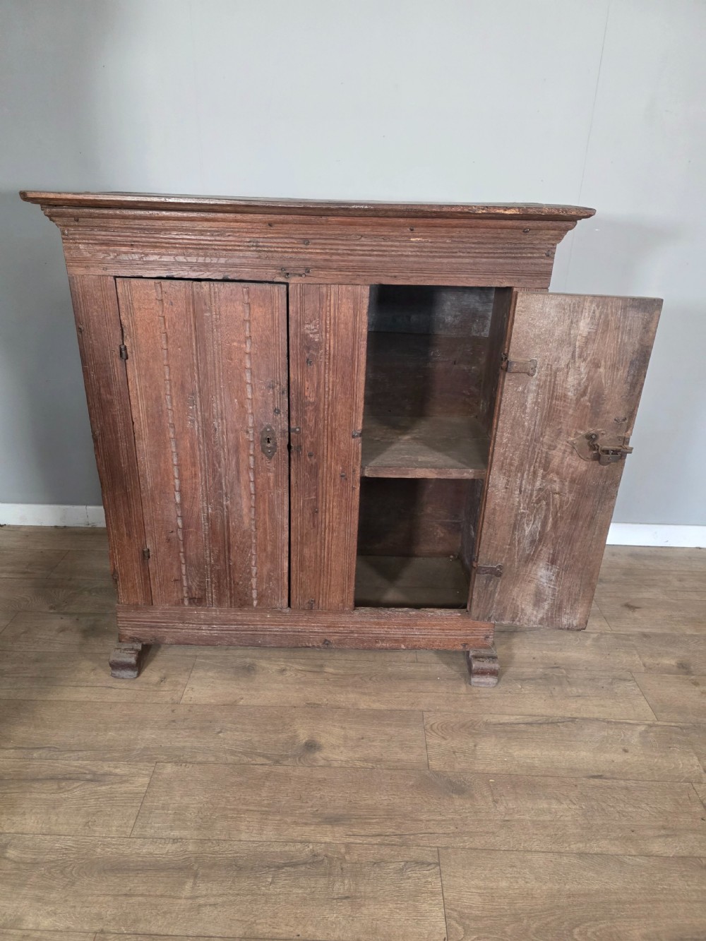 An 18th-century primitive dark oak cupboard featuring two panelled doors with notch carving, wrought iron escutcheons, and moulded top cornicing. View VIII