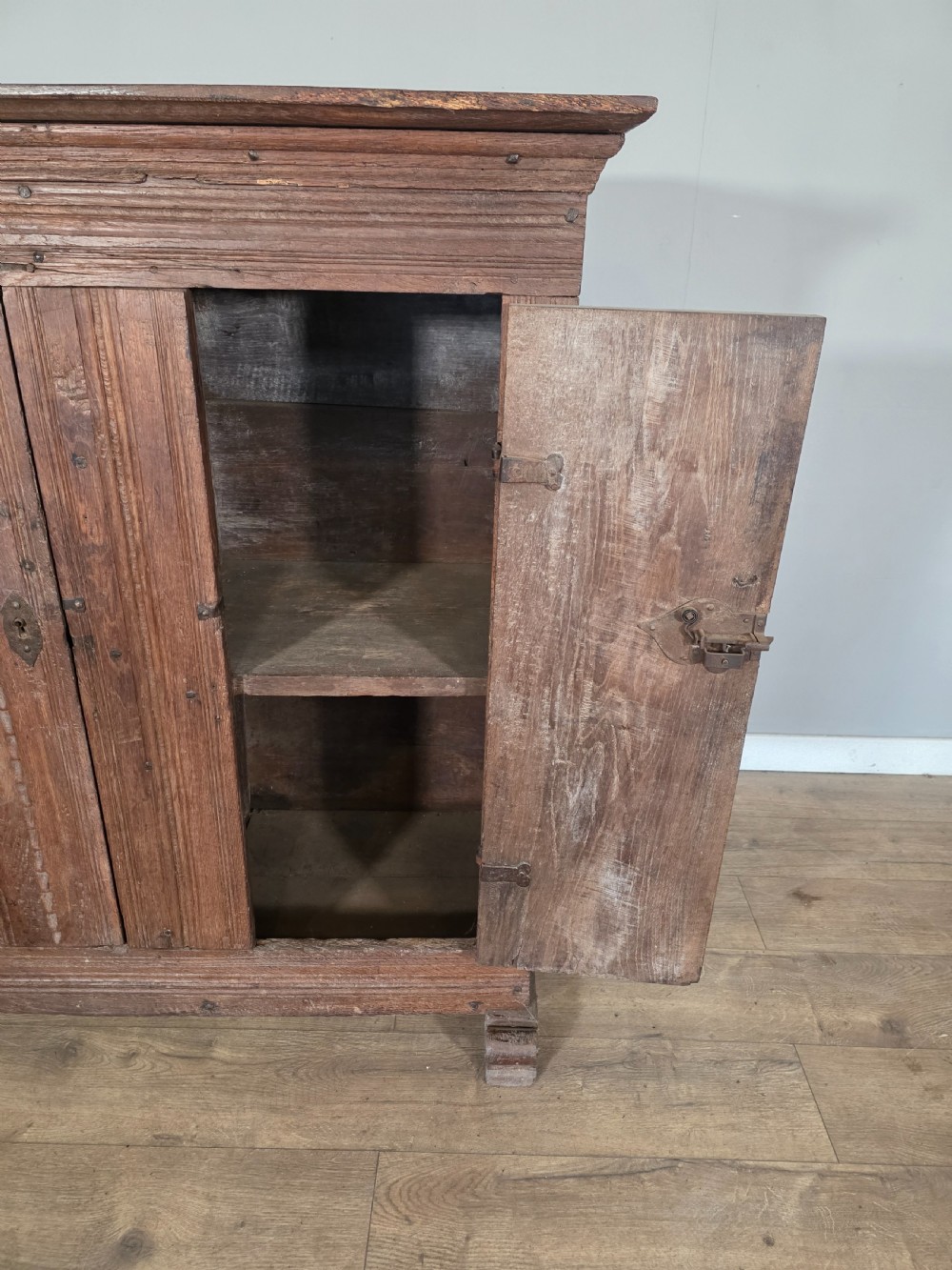 An 18th-century primitive dark oak cupboard featuring two panelled doors with notch carving, wrought iron escutcheons, and moulded top cornicing. View X