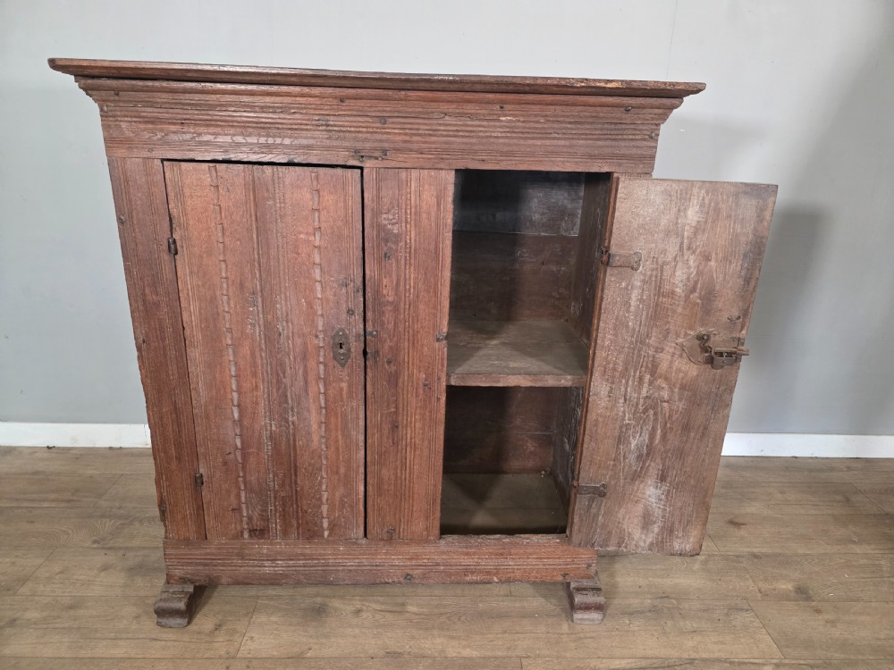An 18th-century primitive dark oak cupboard featuring two panelled doors with notch carving, wrought iron escutcheons, and moulded top cornicing. View XI