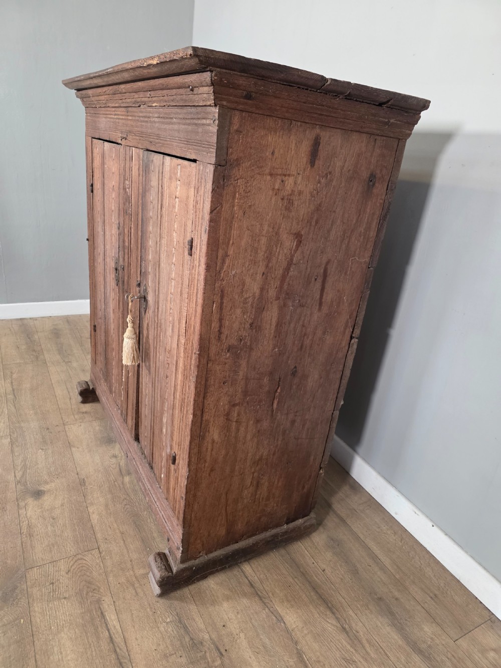 An 18th-century primitive dark oak cupboard featuring two panelled doors with notch carving, wrought iron escutcheons, and moulded top cornicing. View XII