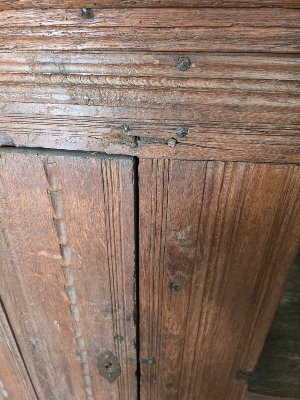 An 18th-century primitive dark oak cupboard featuring two panelled doors with notch carving, wrought iron escutcheons, and moulded top cornicing. View XVII