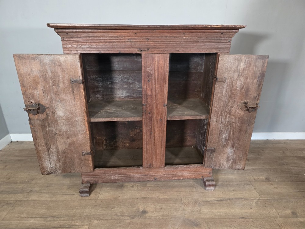 An 18th-century primitive dark oak cupboard featuring two panelled doors with notch carving, wrought iron escutcheons, and moulded top cornicing. View XVIII