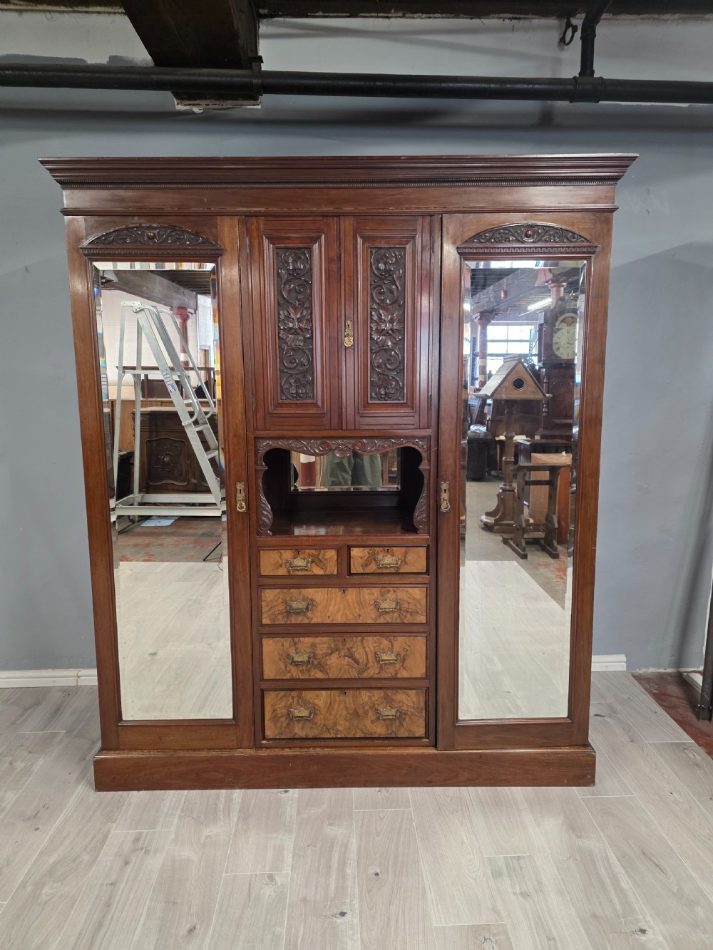 A late Victorian walnut combination wardrobe featuring twin mirrored doors flanking a central section of carved cupboards, an open shelf niche, and five burr walnut drawers.