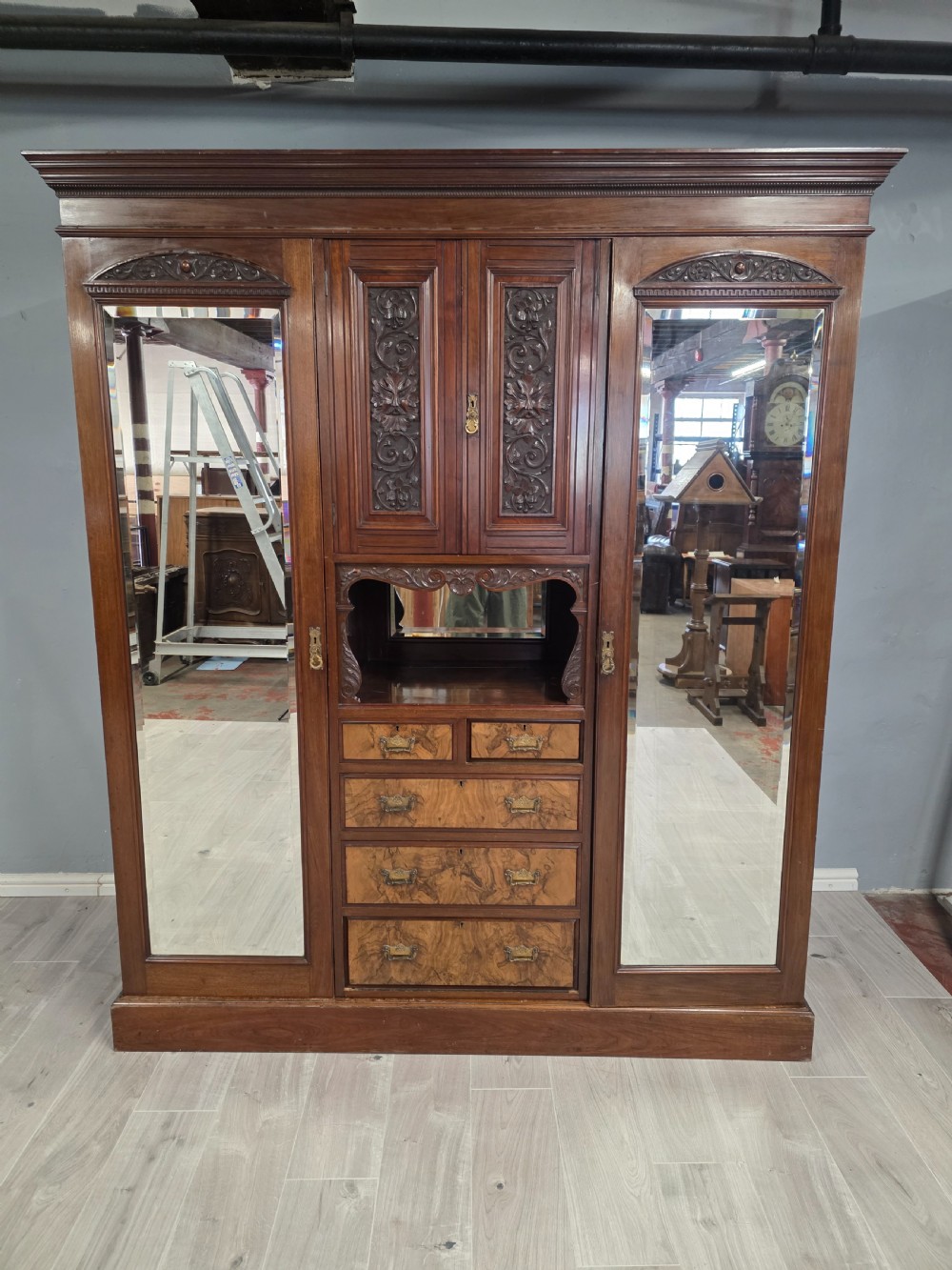A late Victorian walnut combination wardrobe featuring twin mirrored doors flanking a central section of carved cupboards, an open shelf niche, and five burr walnut drawers. View II