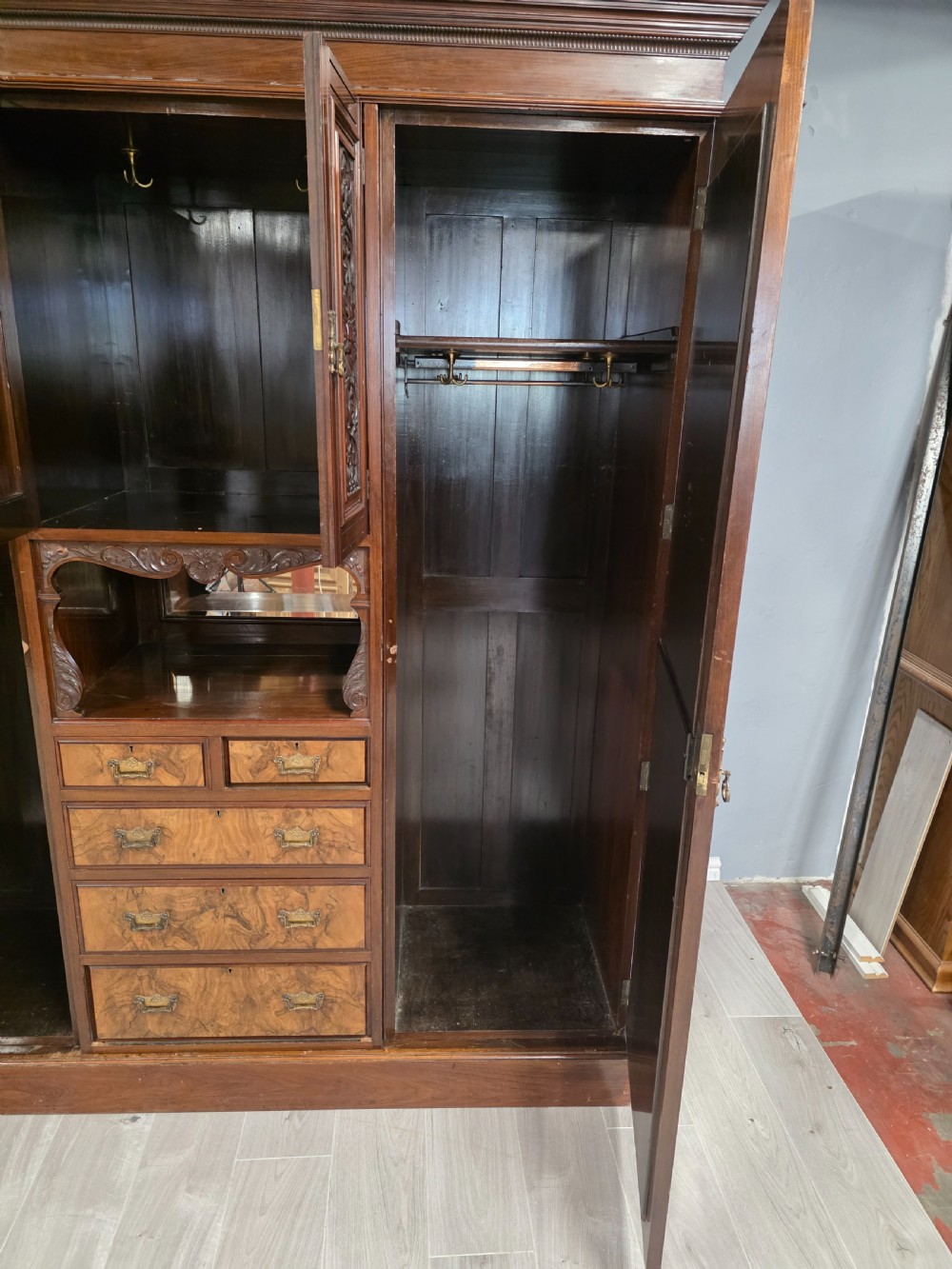A late Victorian walnut combination wardrobe featuring twin mirrored doors flanking a central section of carved cupboards, an open shelf niche, and five burr walnut drawers. View VI