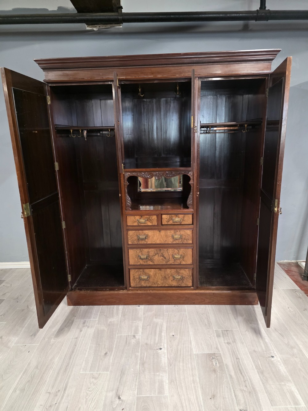 A late Victorian walnut combination wardrobe featuring twin mirrored doors flanking a central section of carved cupboards, an open shelf niche, and five burr walnut drawers. View VII