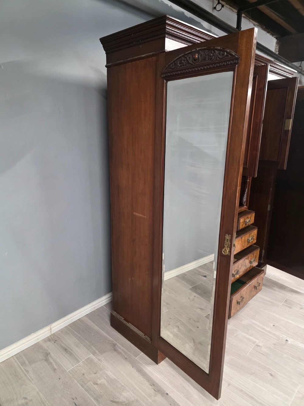 A late Victorian walnut combination wardrobe featuring twin mirrored doors flanking a central section of carved cupboards, an open shelf niche, and five burr walnut drawers. View IX