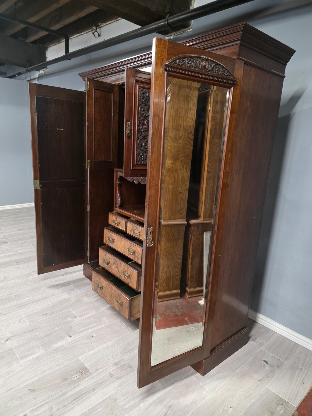 A late Victorian walnut combination wardrobe featuring twin mirrored doors flanking a central section of carved cupboards, an open shelf niche, and five burr walnut drawers. View X