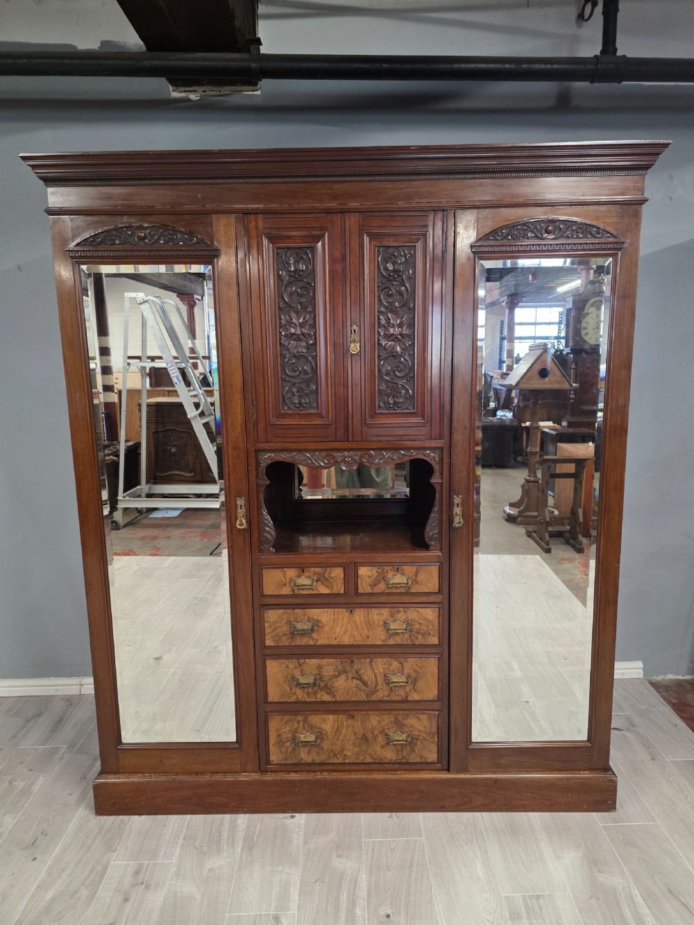 A late Victorian walnut combination wardrobe featuring twin mirrored doors flanking a central section of carved cupboards, an open shelf niche, and five burr walnut drawers. View XIV