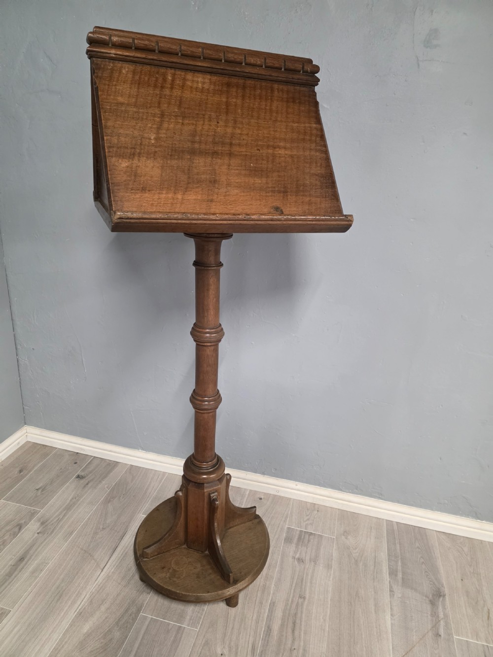 An antique Victorian oak church lectern featuring a sloped book rest with dentil moulding, a turned central column, and a circular base with bracket supports. View II
