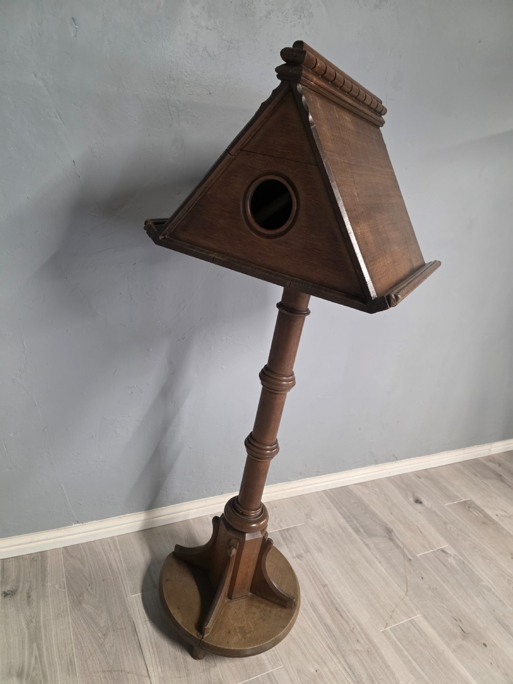 An antique Victorian oak church lectern featuring a sloped book rest with dentil moulding, a turned central column, and a circular base with bracket supports. View IV