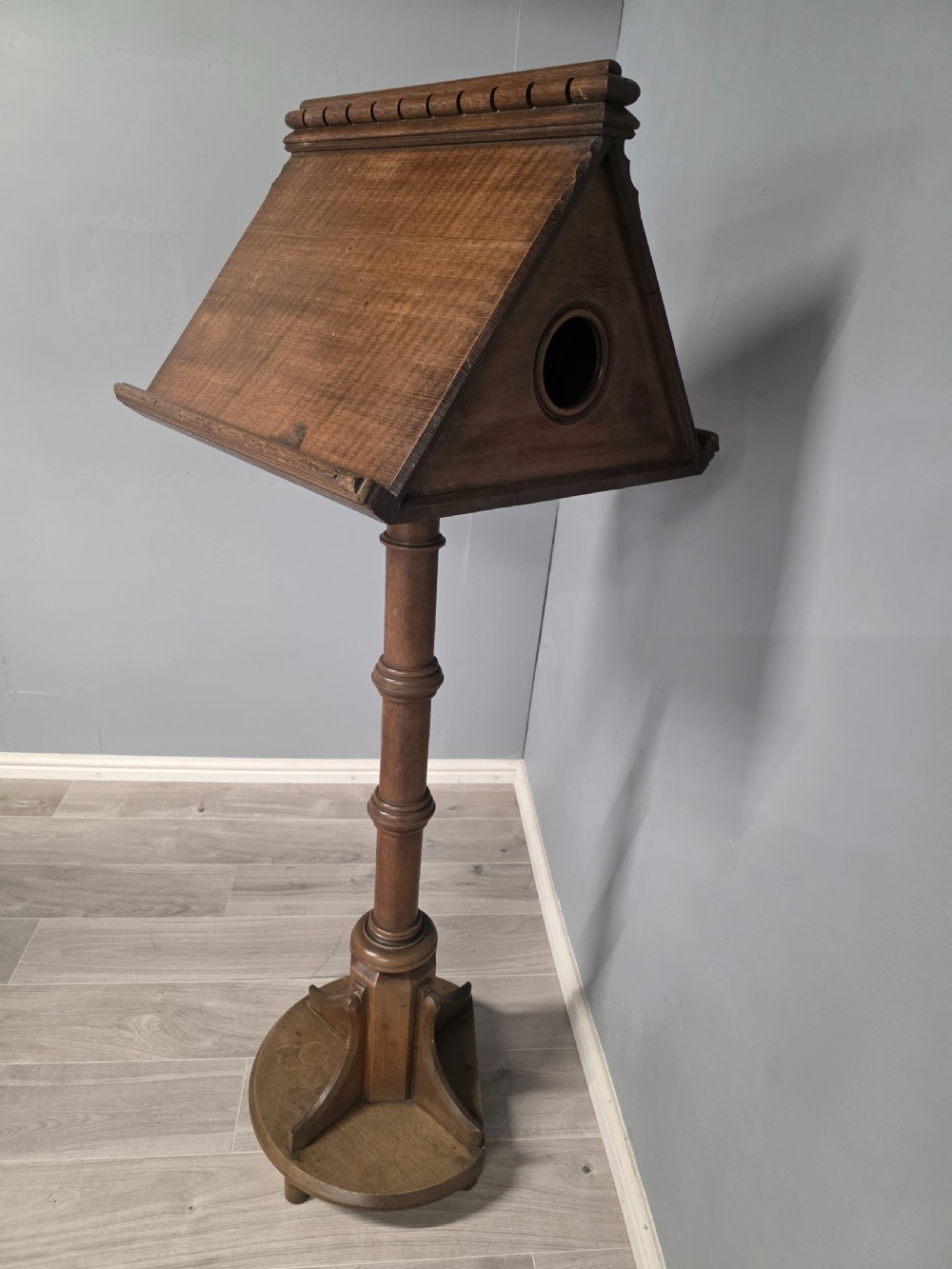 An antique Victorian oak church lectern featuring a sloped book rest with dentil moulding, a turned central column, and a circular base with bracket supports. View V
