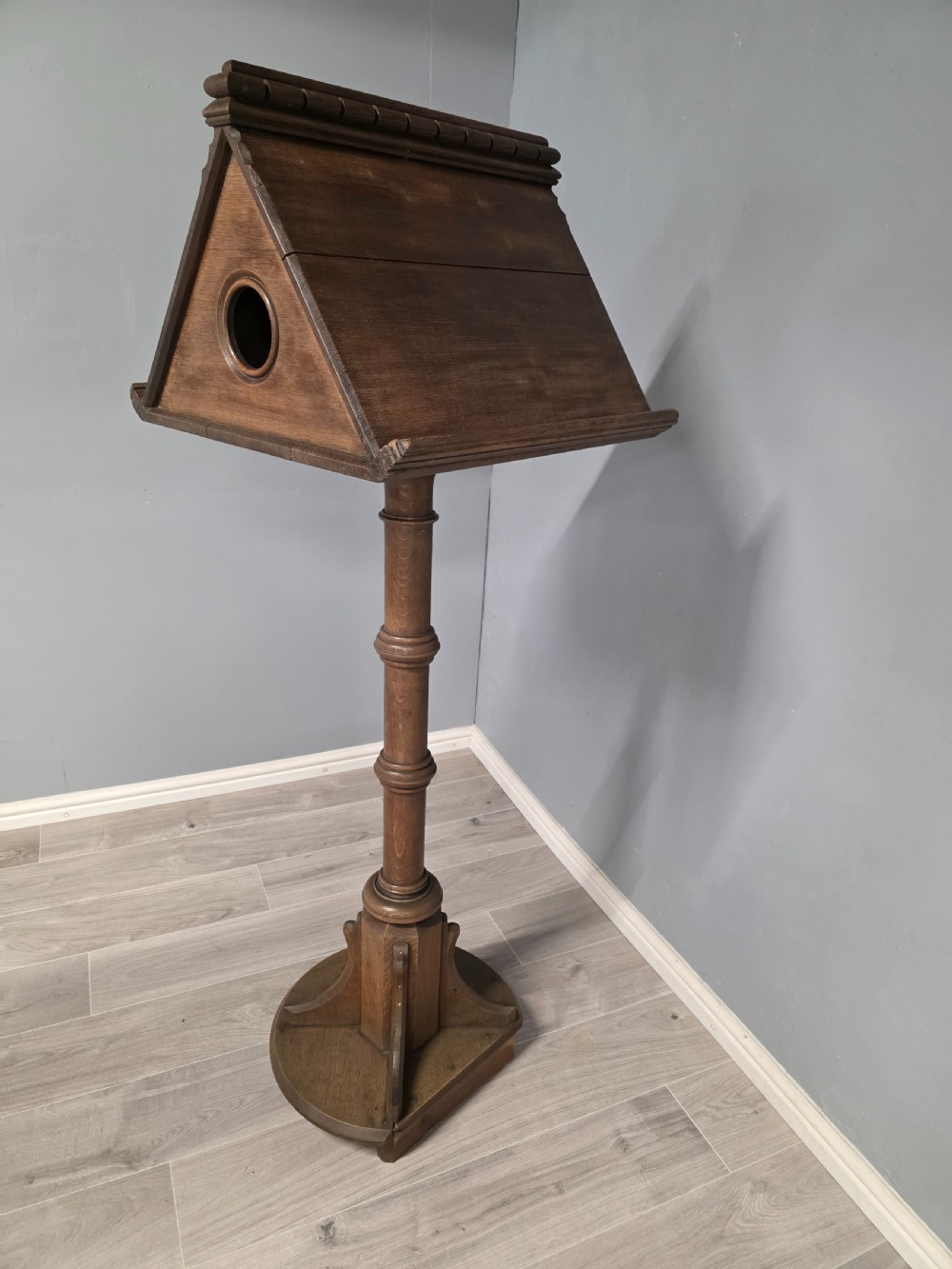 An antique Victorian oak church lectern featuring a sloped book rest with dentil moulding, a turned central column, and a circular base with bracket supports. View VI