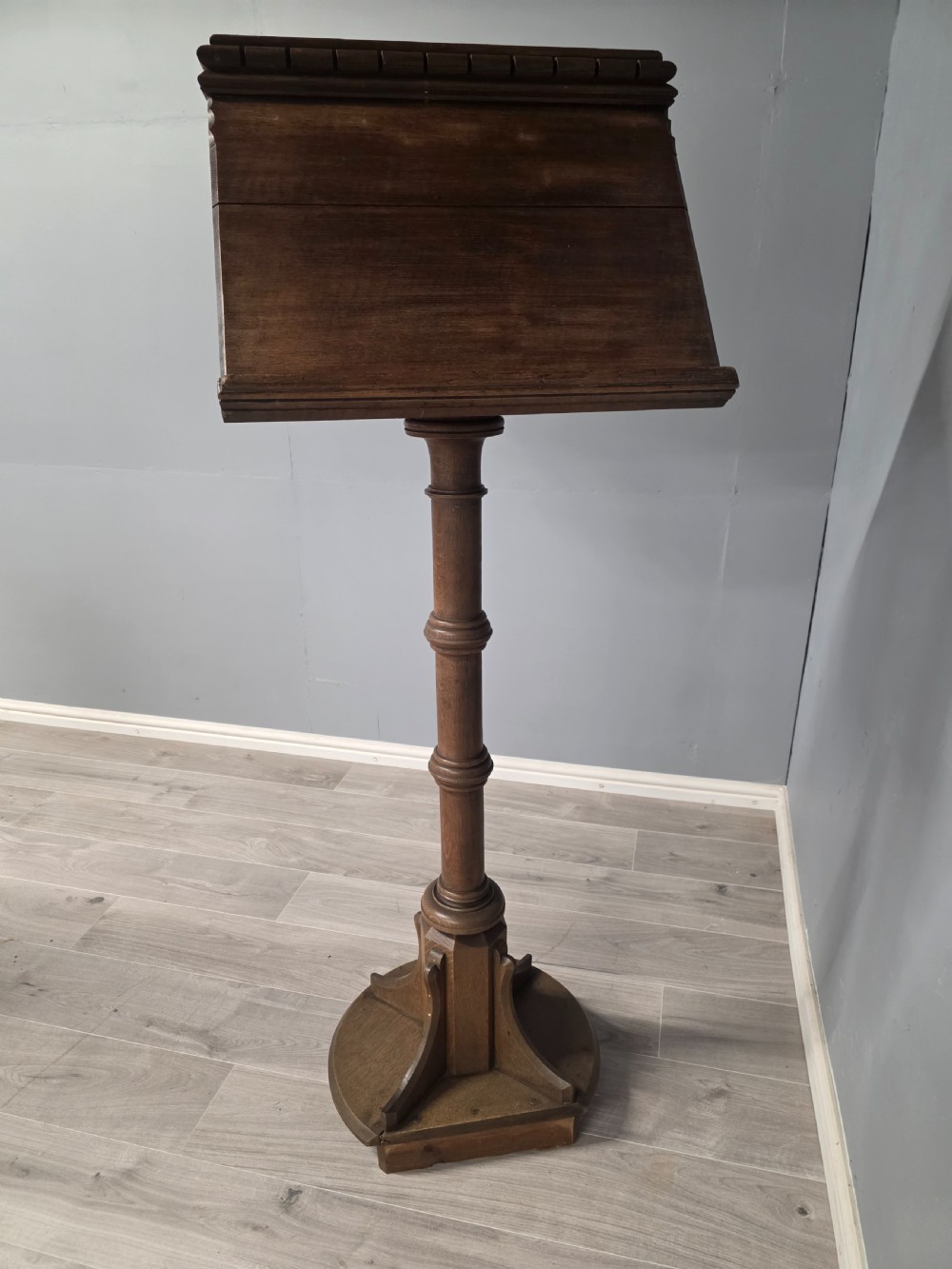 An antique Victorian oak church lectern featuring a sloped book rest with dentil moulding, a turned central column, and a circular base with bracket supports. View VII