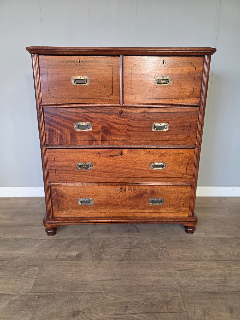 A 19th-century teak military campaign chest of drawers featuring a two-part split design with flush brass handles and turned feet. View II