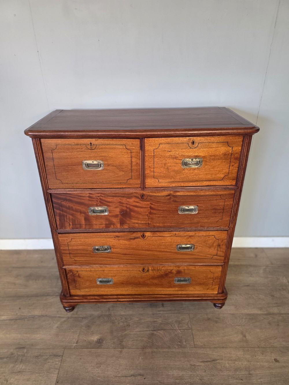 A 19th-century teak military campaign chest of drawers featuring a two-part split design with flush brass handles and turned feet. View IV