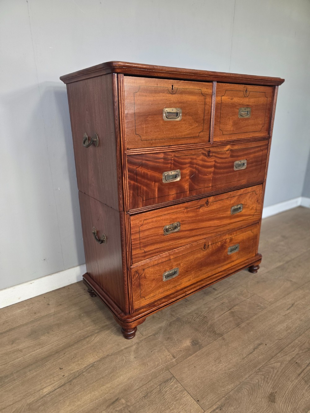A 19th-century teak military campaign chest of drawers featuring a two-part split design with flush brass handles and turned feet. View V