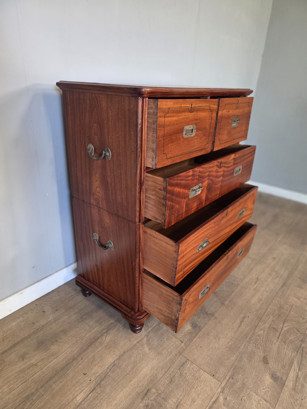 A 19th-century teak military campaign chest of drawers featuring a two-part split design with flush brass handles and turned feet. View VI
