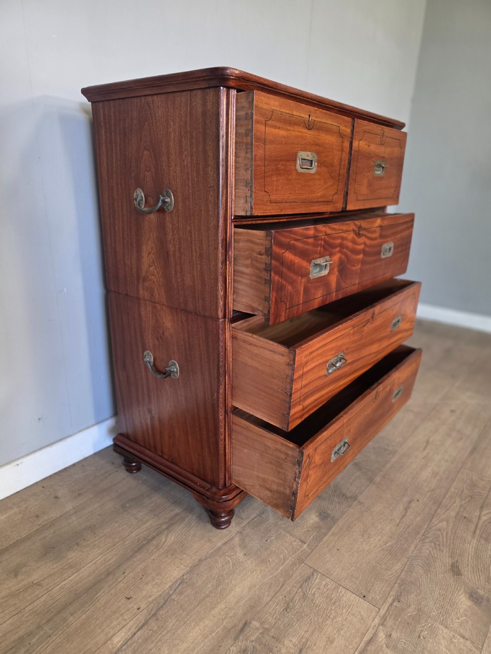 A 19th-century teak military campaign chest of drawers featuring a two-part split design with flush brass handles and turned feet. View VII