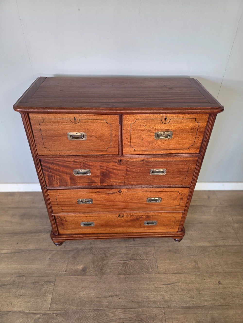 A 19th-century teak military campaign chest of drawers featuring a two-part split design with flush brass handles and turned feet. View IX