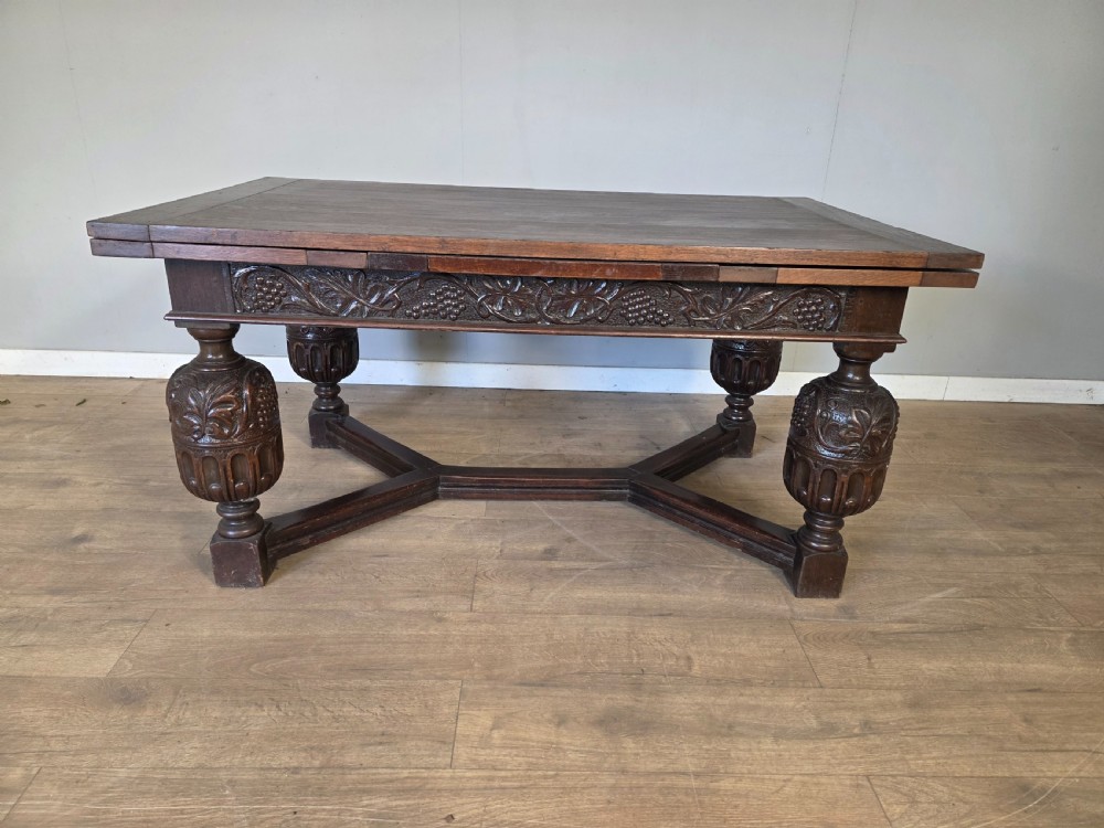 A solid dark oak extending dining table featuring carved bulbous legs, a decorative foliage apron, and a stretcher base.
