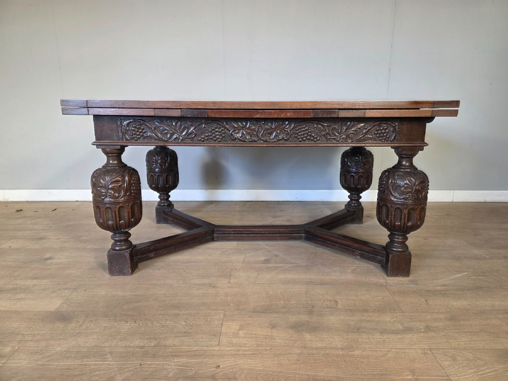 A solid dark oak extending dining table featuring carved bulbous legs, a decorative foliage apron, and a stretcher base. View II