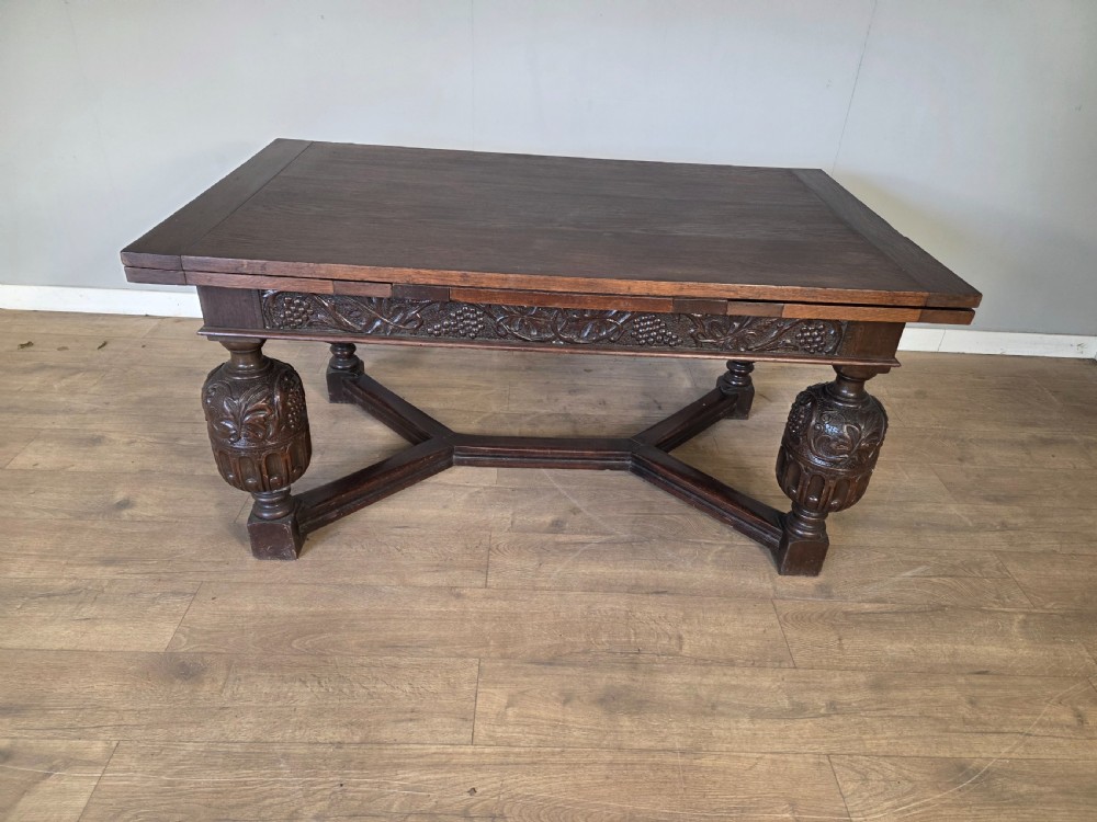 A solid dark oak extending dining table featuring carved bulbous legs, a decorative foliage apron, and a stretcher base. View III