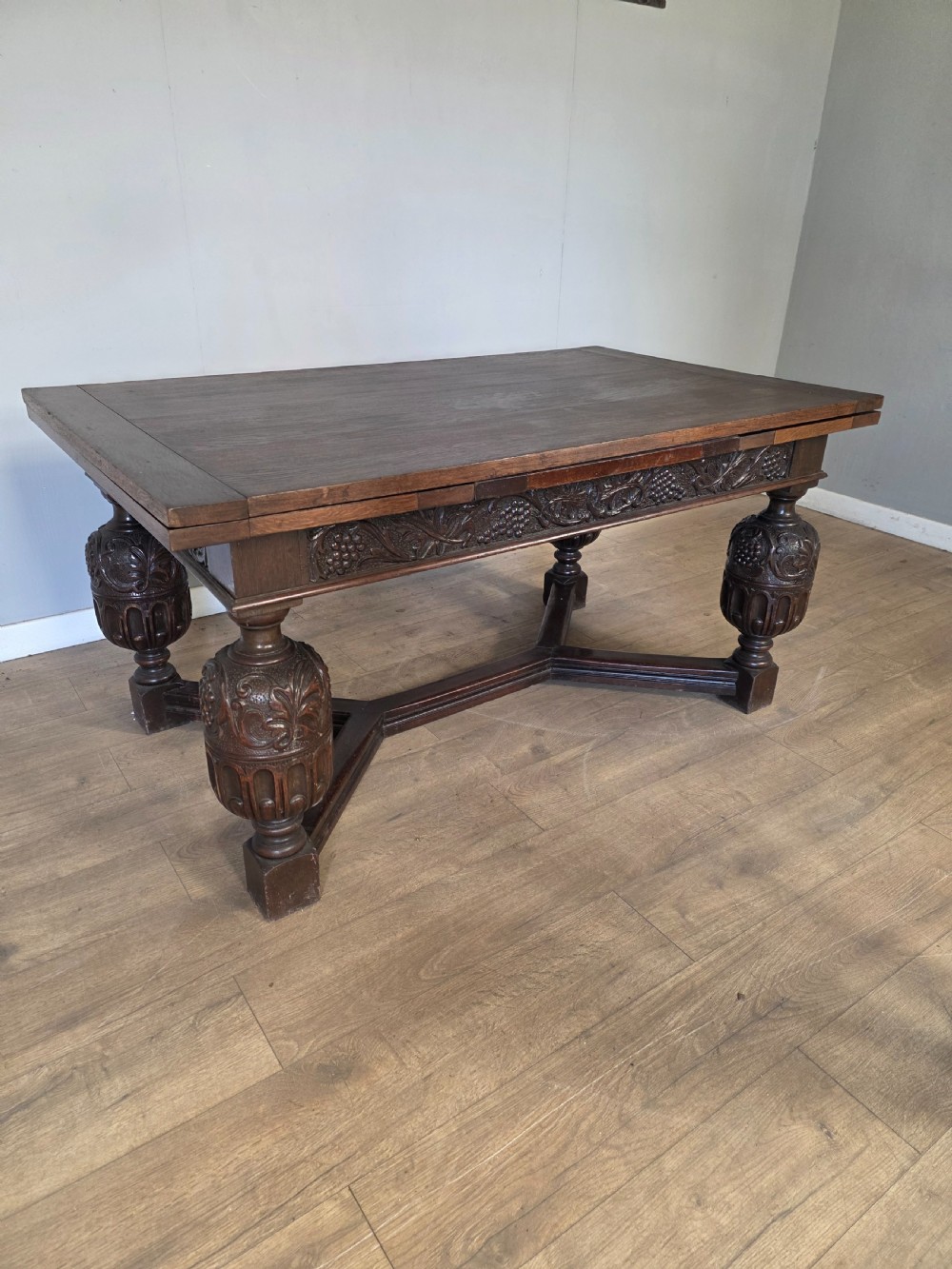 A solid dark oak extending dining table featuring carved bulbous legs, a decorative foliage apron, and a stretcher base. View IV