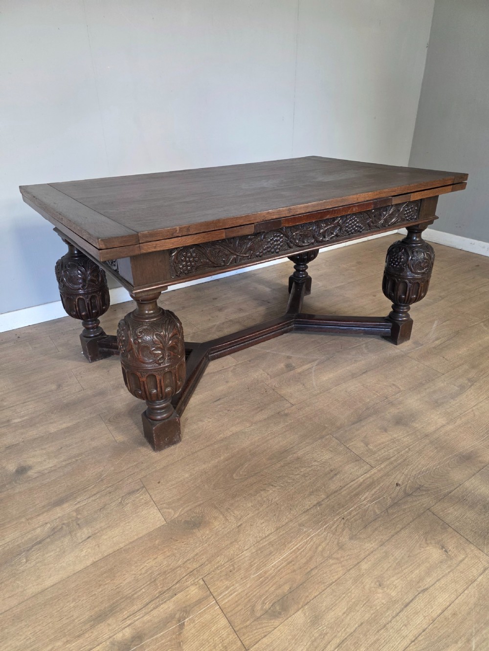 A solid dark oak extending dining table featuring carved bulbous legs, a decorative foliage apron, and a stretcher base. View V