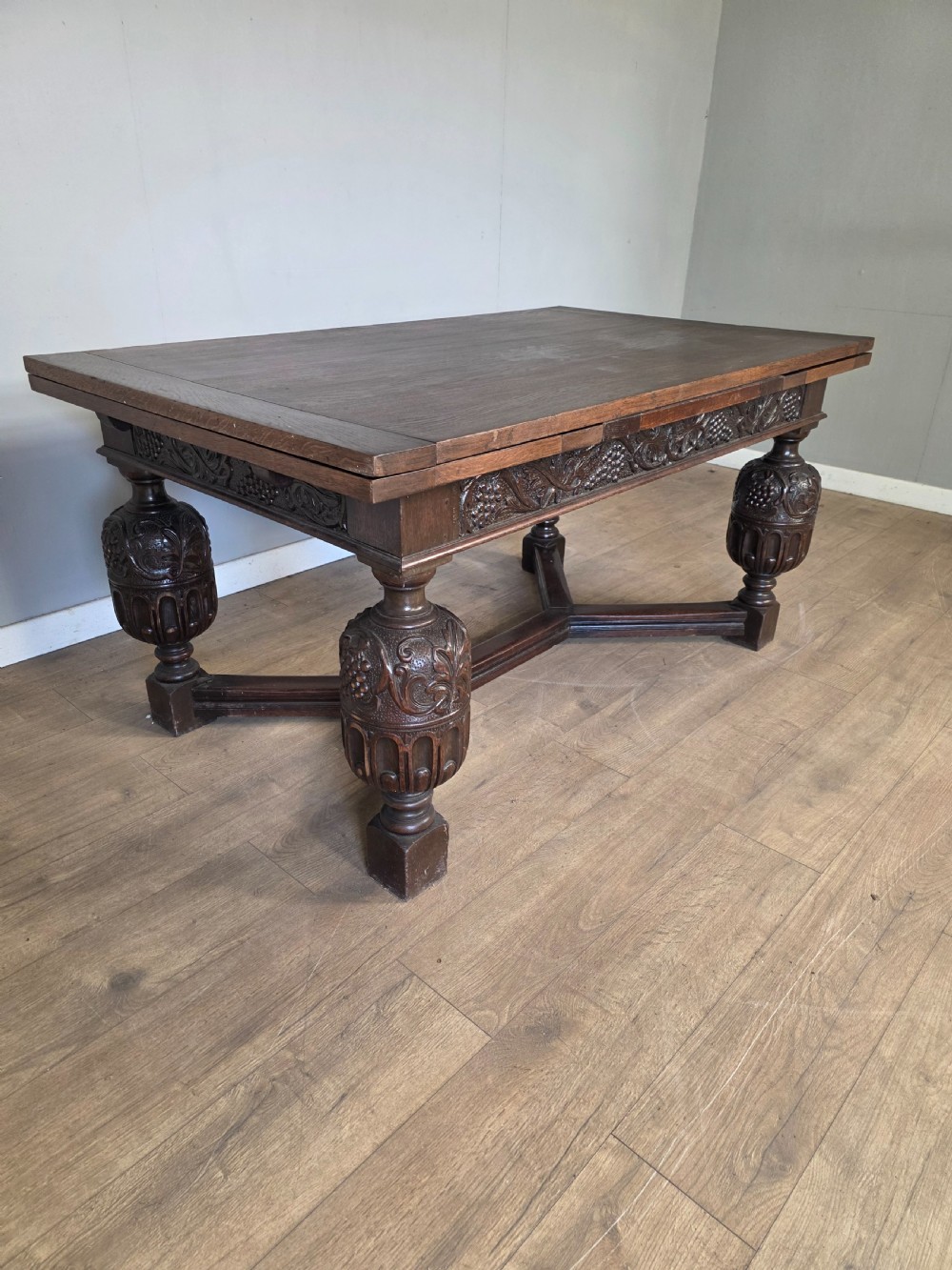 A solid dark oak extending dining table featuring carved bulbous legs, a decorative foliage apron, and a stretcher base. View VI