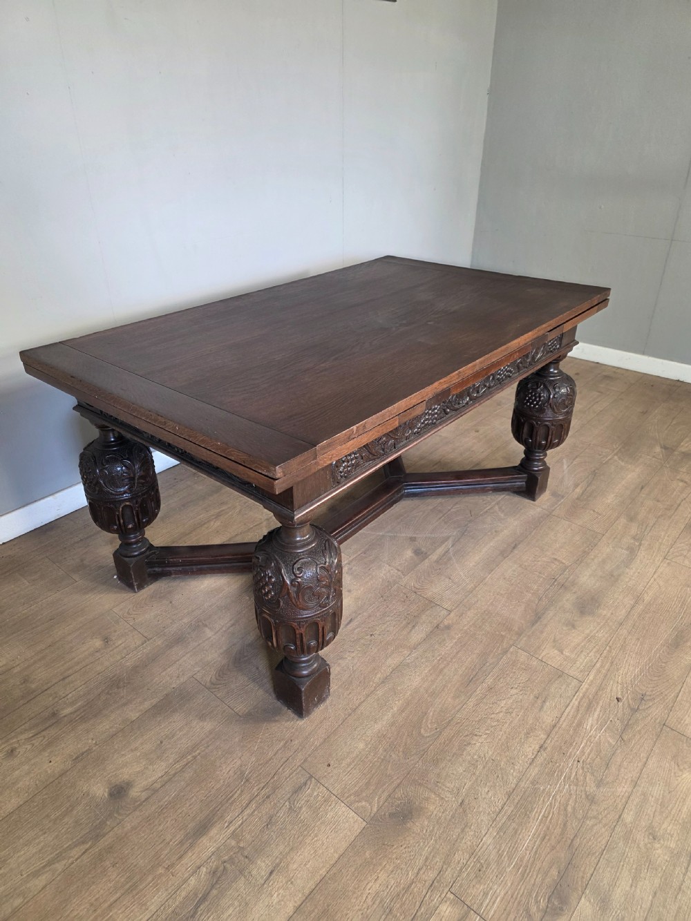 A solid dark oak extending dining table featuring carved bulbous legs, a decorative foliage apron, and a stretcher base. View VII