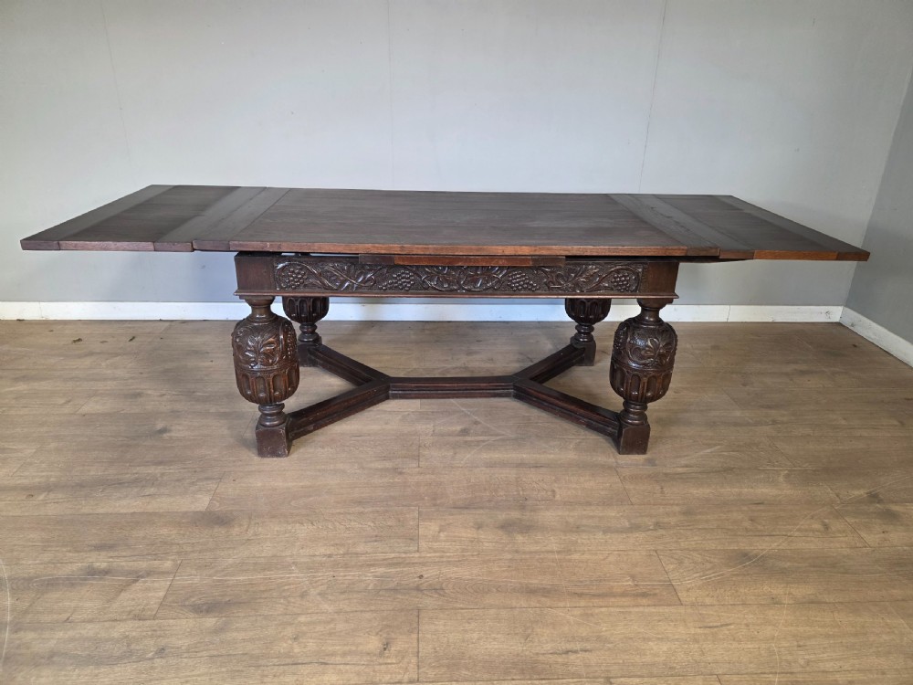 A solid dark oak extending dining table featuring carved bulbous legs, a decorative foliage apron, and a stretcher base. View VIII