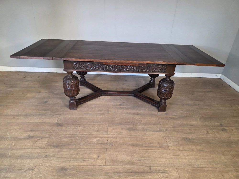 A solid dark oak extending dining table featuring carved bulbous legs, a decorative foliage apron, and a stretcher base. View IX