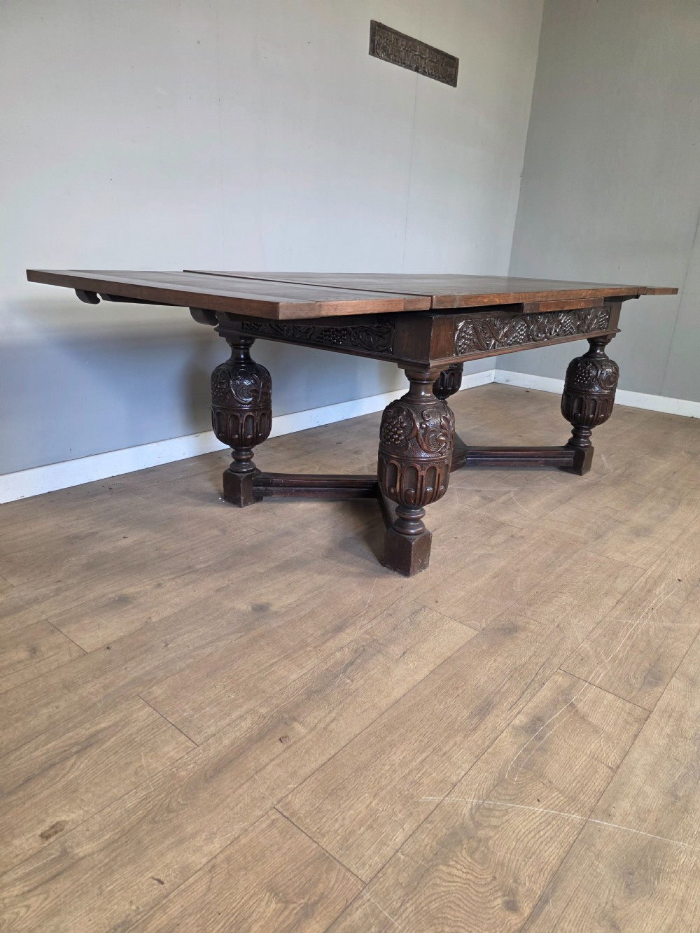 A solid dark oak extending dining table featuring carved bulbous legs, a decorative foliage apron, and a stretcher base. View XI