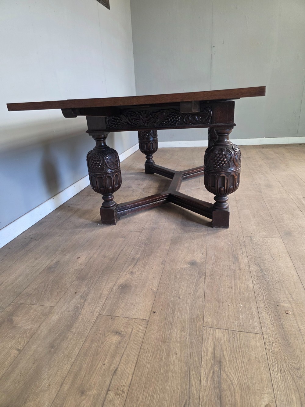 A solid dark oak extending dining table featuring carved bulbous legs, a decorative foliage apron, and a stretcher base. View XV