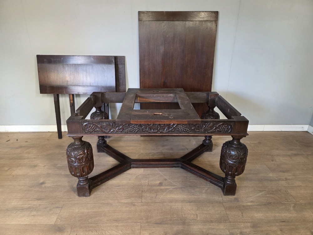 A solid dark oak extending dining table featuring carved bulbous legs, a decorative foliage apron, and a stretcher base. View XVI